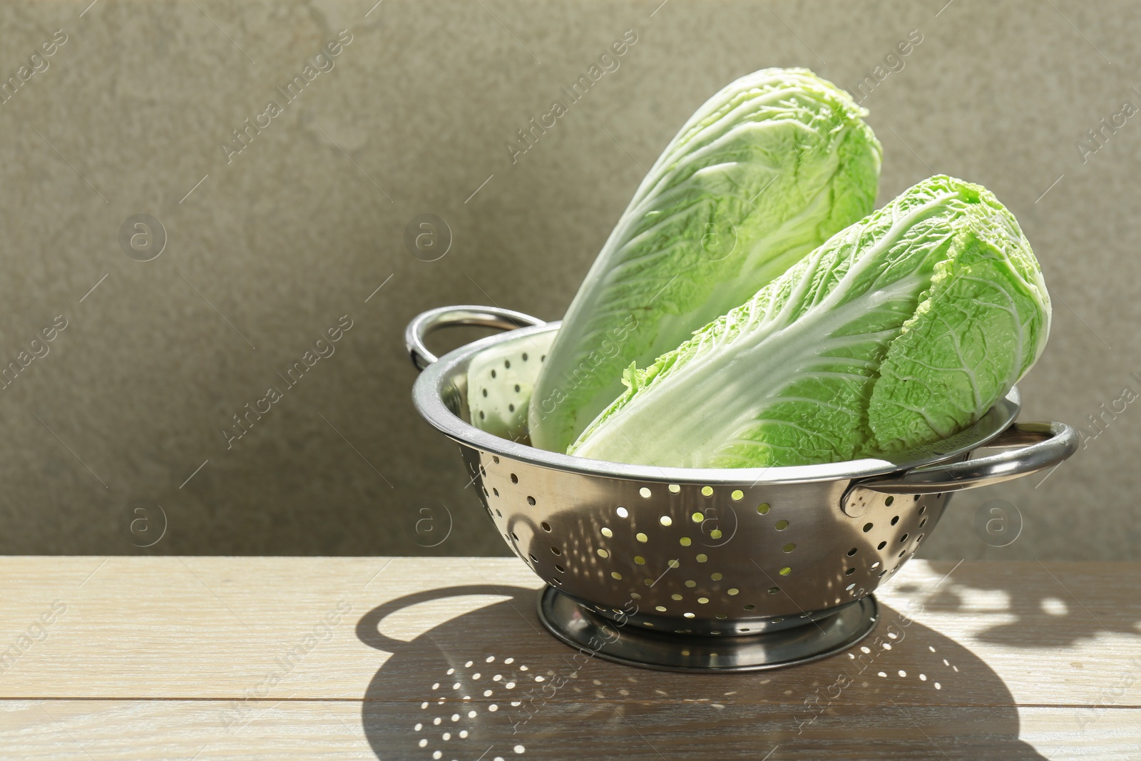 Photo of Fresh Chinese cabbages in colander on light wooden table indoors. Space for text