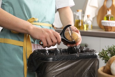 Photo of Woman peeling fresh potato above garbage bin indoors, closeup