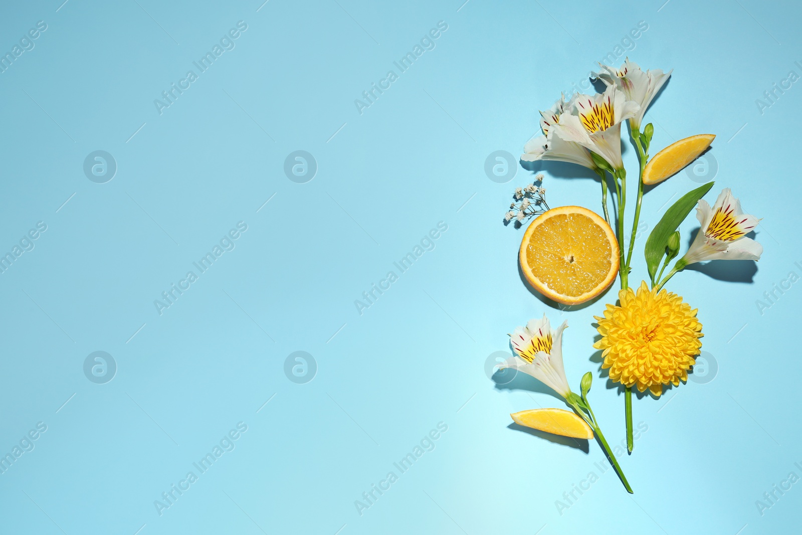 Photo of Flat lay composition with alstroemeria flowers and orange slices on light blue background, space for text