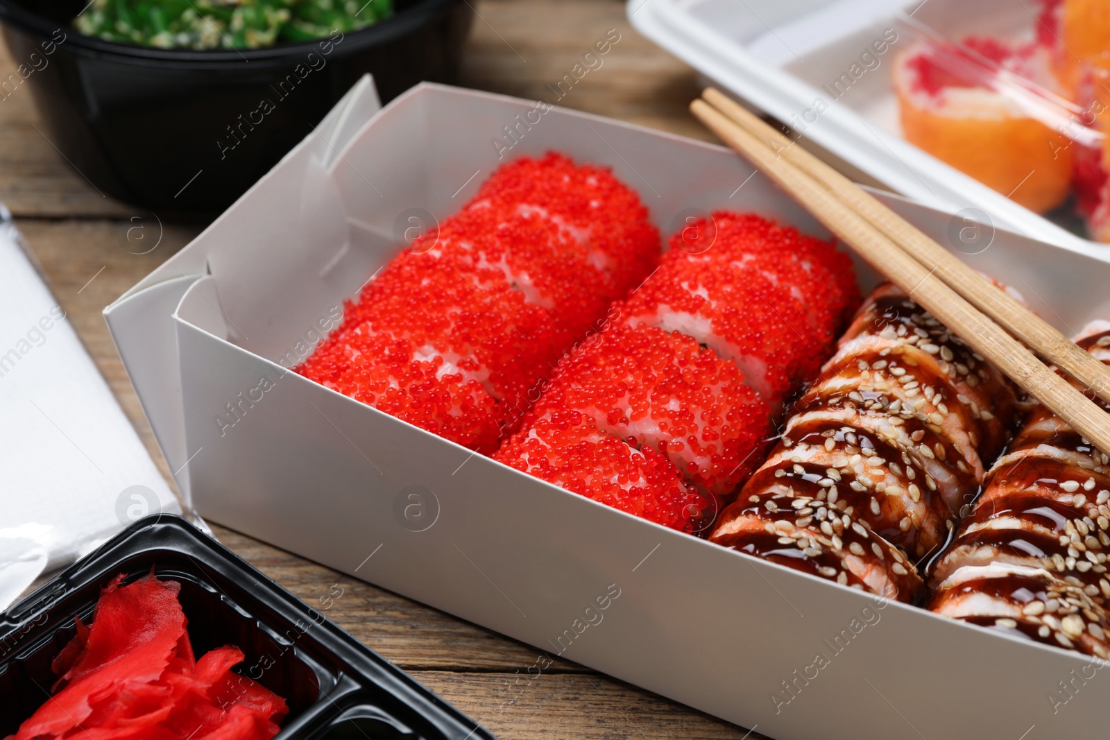 Photo of Paper box with delicious sushi rolls on wooden table, closeup. Food delivery