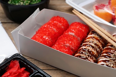 Photo of Paper box with delicious sushi rolls on wooden table, closeup. Food delivery
