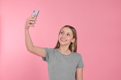 Teenage girl taking selfie on pink background