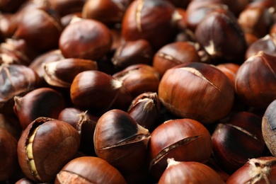 Photo of Pile of delicious edible roasted chestnuts as background, closeup