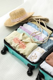Photo of Open suitcase packed for trip and accessories on bed