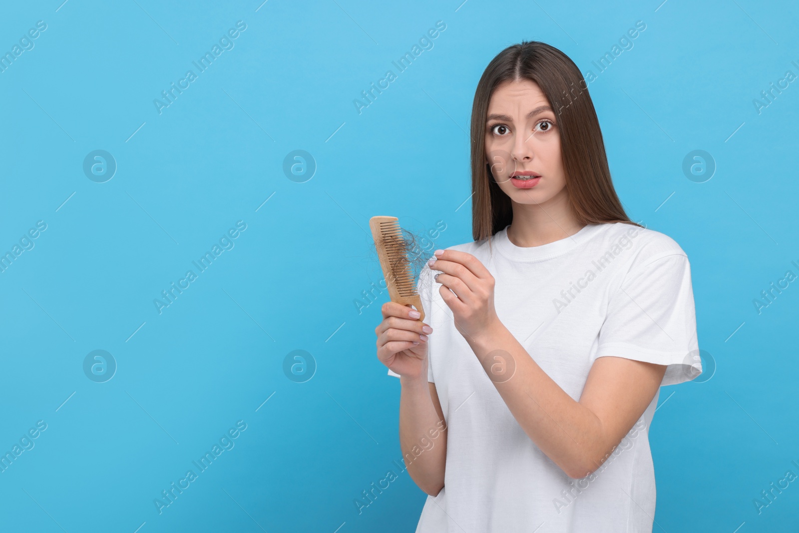 Photo of Emotional woman untangling her lost hair from comb on light blue background, space for text. Alopecia problem