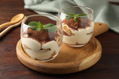 Photo of Delicious tiramisu in glasses and mint leaves on wooden table