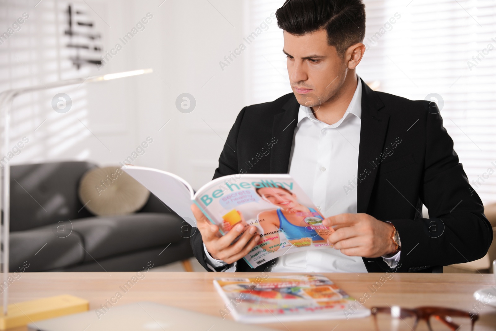 Photo of Man reading magazine at table in office