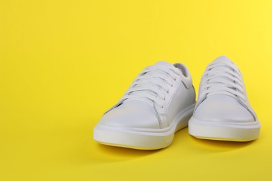 Photo of Pair of stylish white sneakers on yellow background, space for text