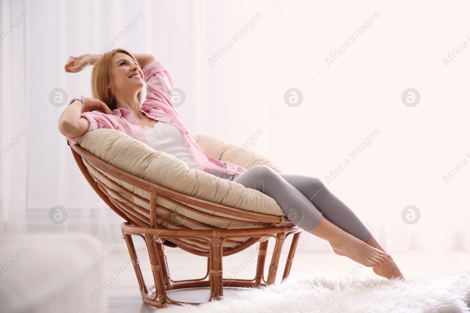 Photo of Young woman relaxing in papasan chair near window at home