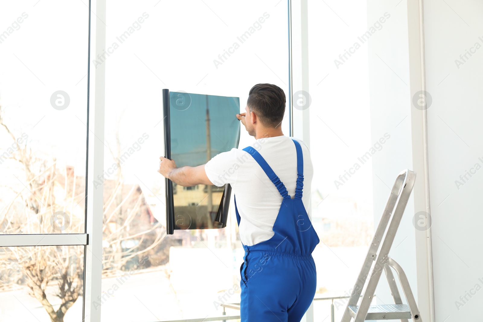 Photo of Professional worker tinting window with foil indoors