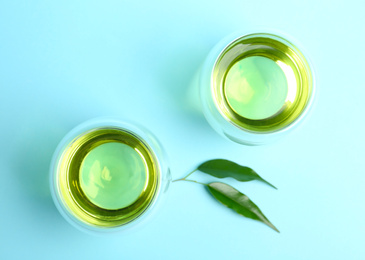 Photo of Aromatic green tea and leaves on light blue background, flat lay