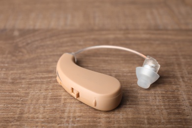 Photo of Hearing aid on wooden table, closeup. Medical device