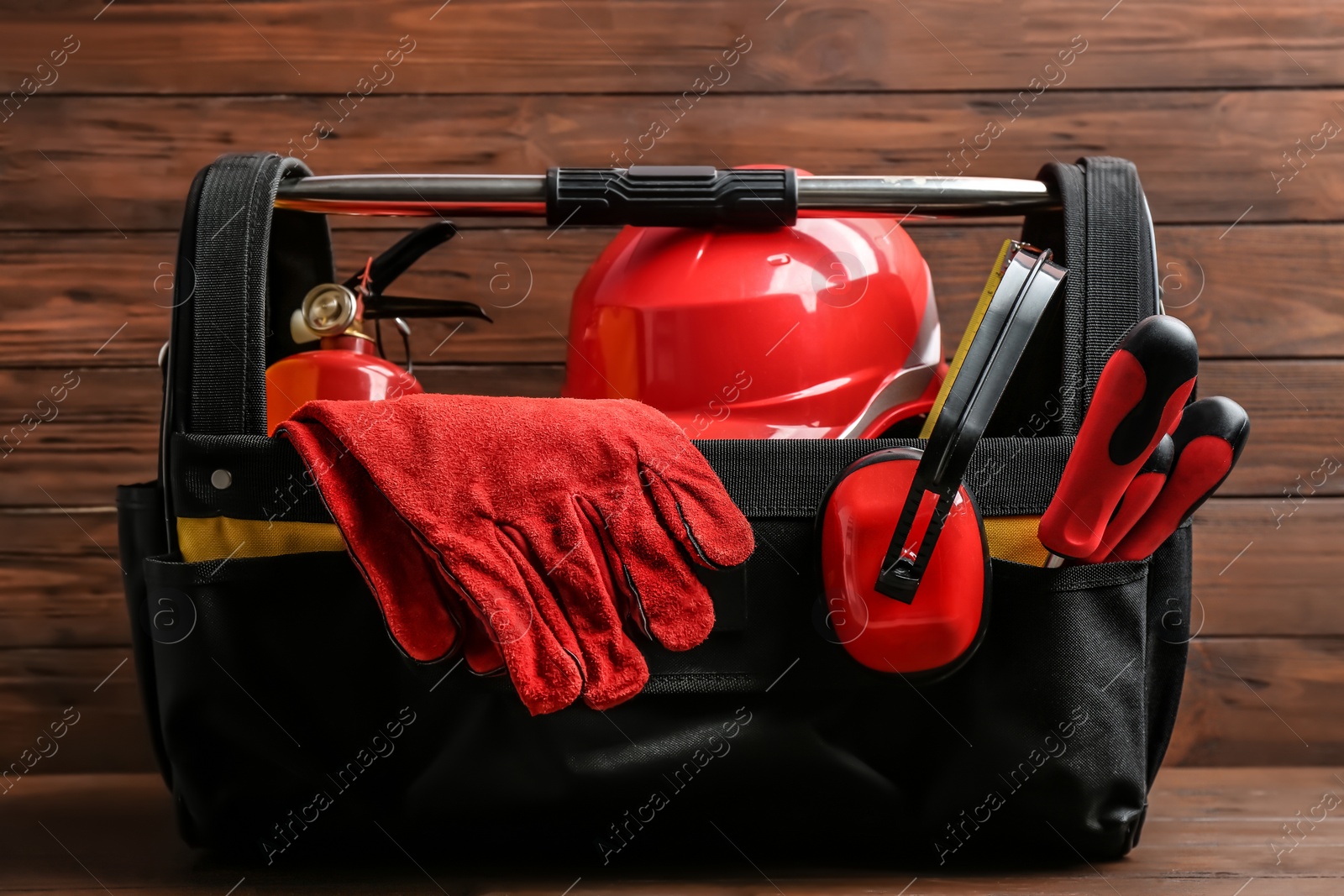 Photo of Black bag with construction tools on table against wooden background