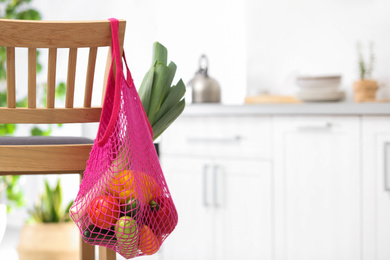 Photo of Net bag with vegetables hanging on wooden chair in kitchen. Space for text