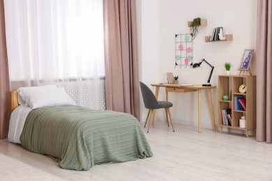 Comfortable bed, wooden desk and shelves near window in bedroom. Interior design