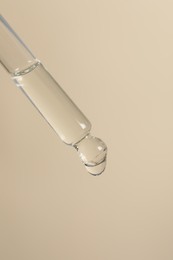 Dripping cosmetic serum from pipette on beige background