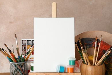 Wooden easel with blank canvas board and painting tools for children on color background