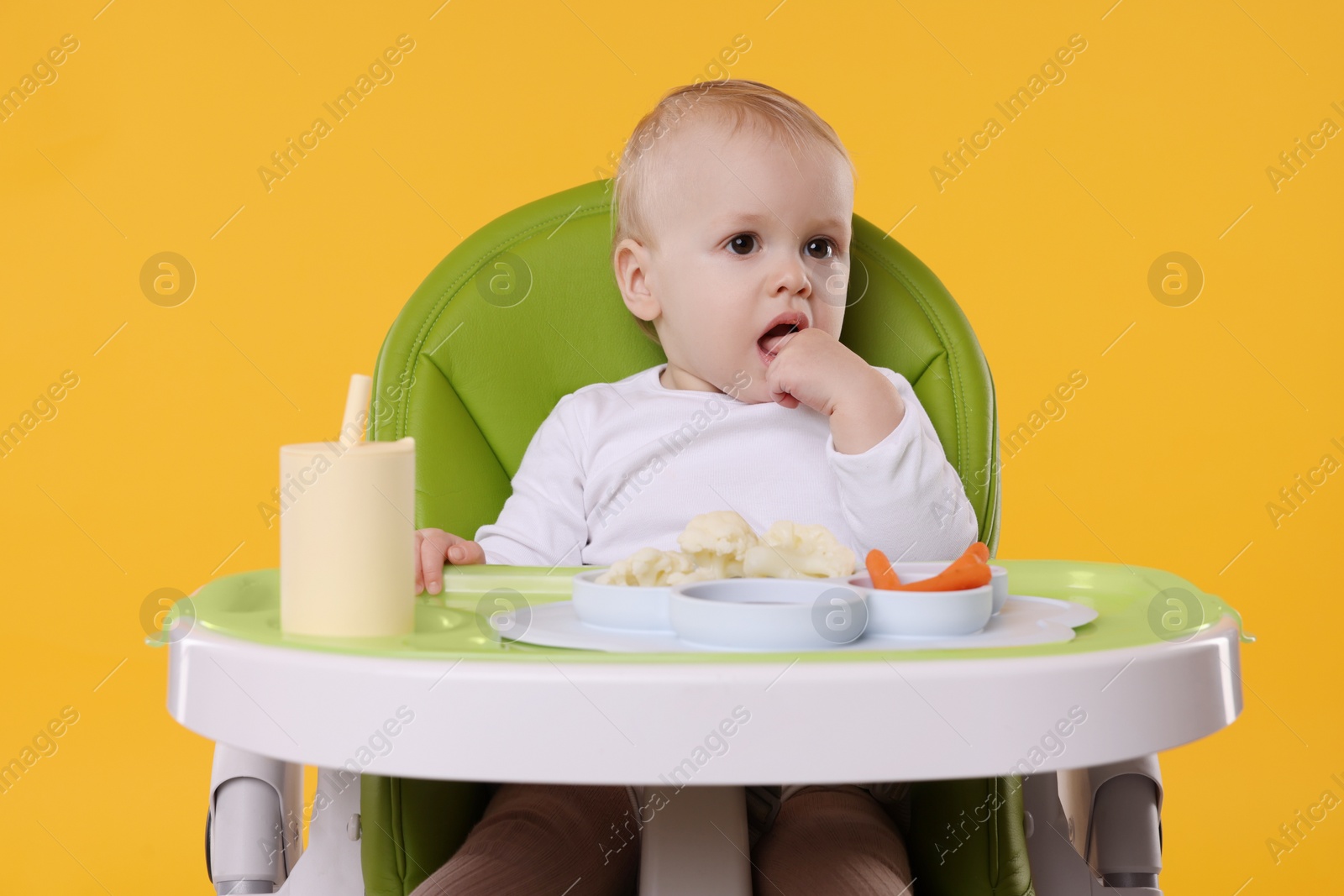 Photo of Cute little baby with healthy food in high chair on orange background