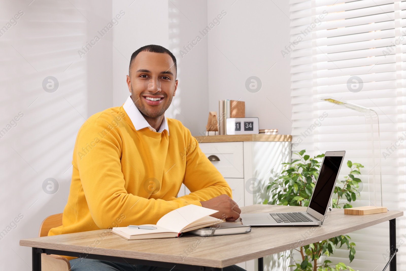 Photo of Young man sitting at desk in room. Home office