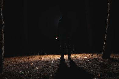 Photo of Silhouette of man with bright flashlight in forest at night