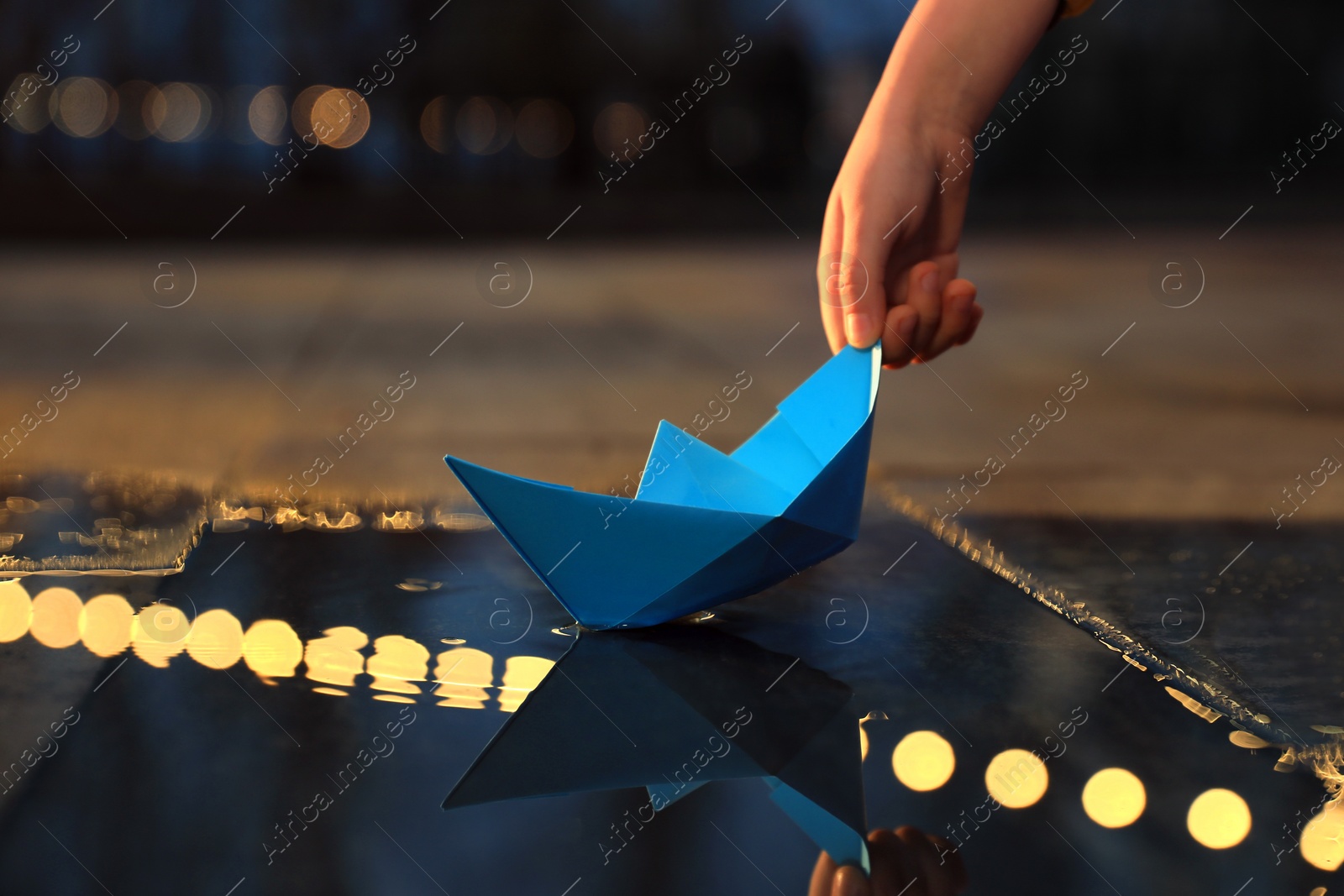 Photo of Little boy playing with paper boat near puddle outdoors, closeup