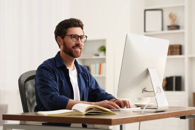 Home workplace. Happy man working with computer at wooden desk in room