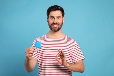 Photo of Happy man with condom showing ok gesture on light blue background. Safe sex