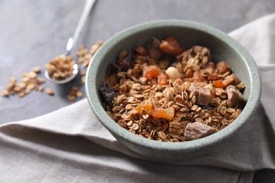 Photo of Tasty granola in bowl and napkin on gray table, closeup