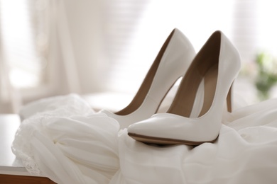 Photo of Pair of white high heel shoes and wedding dress on table indoors