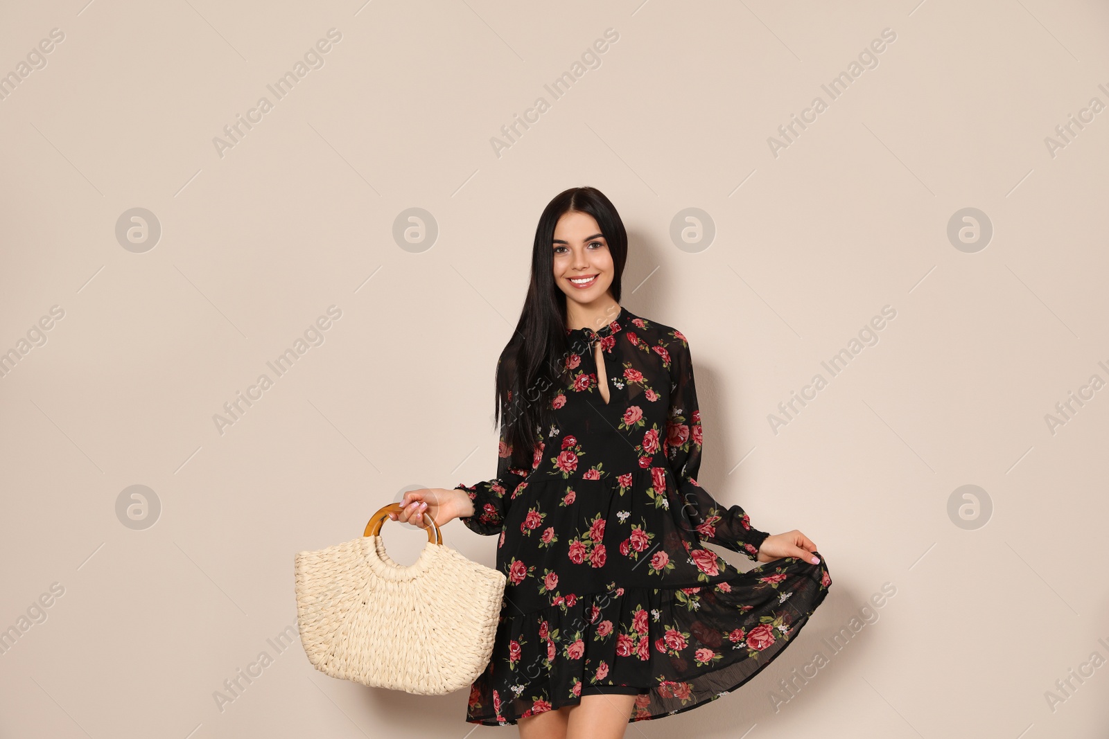 Photo of Young woman wearing floral print dress with straw bag on beige background