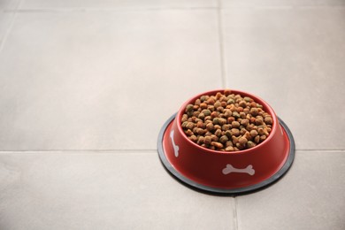 Dry dog food in feeding bowl on tiled floor. Space for text