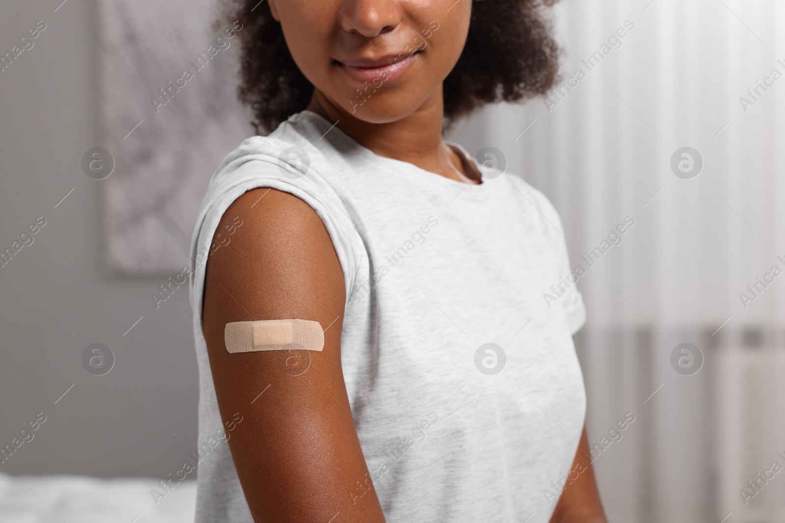 Photo of Young woman with adhesive bandage on her arm after vaccination indoors, closeup