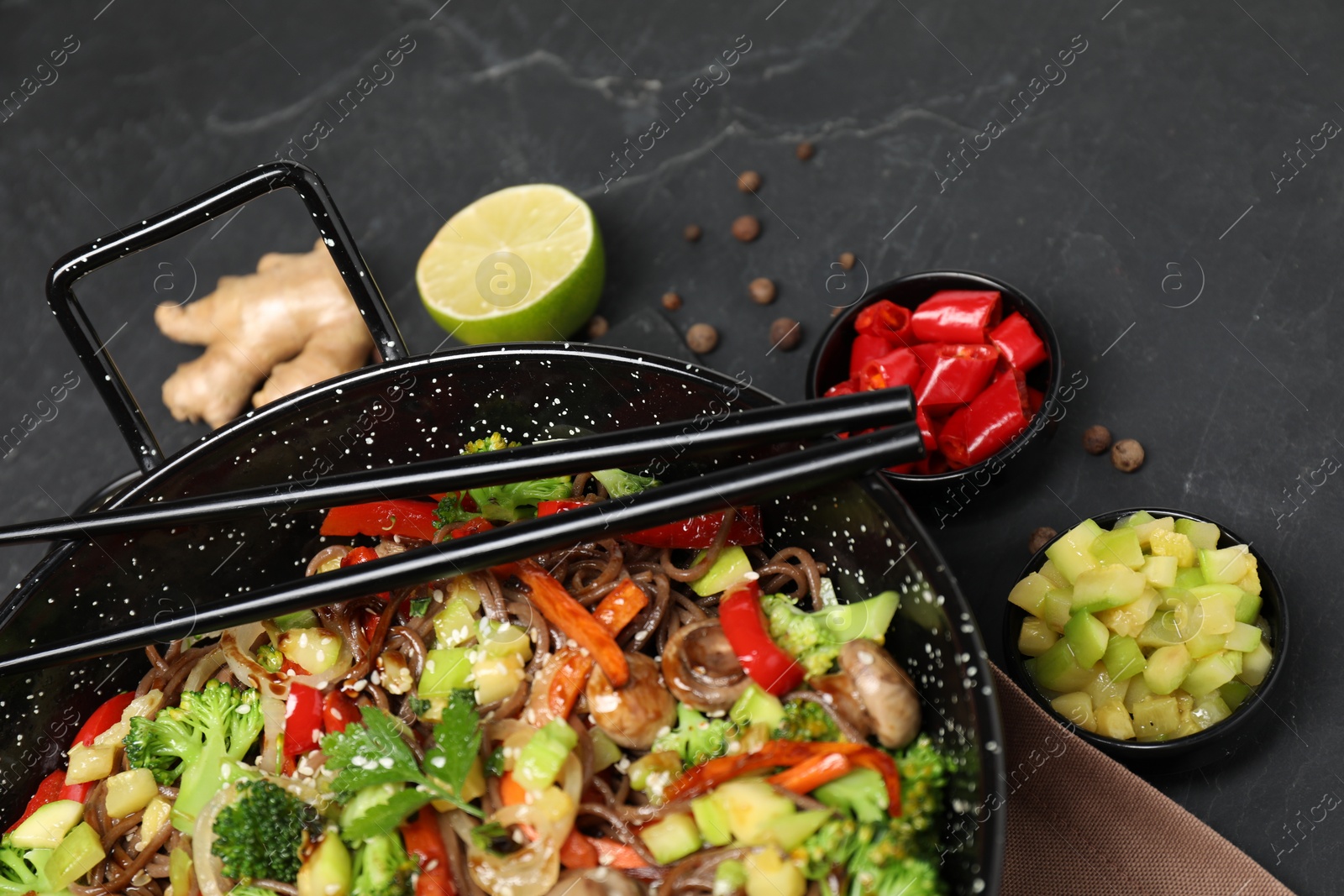 Photo of Wok with noodles, mushrooms, vegetables and other products on black table