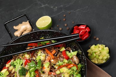 Photo of Wok with noodles, mushrooms, vegetables and other products on black table