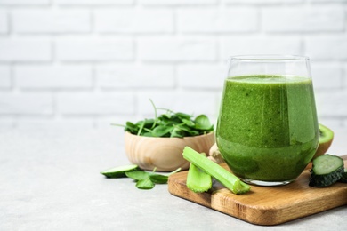 Photo of Delicious green juice and fresh ingredients on table against brick wall, space for text