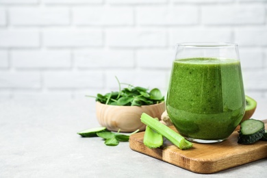 Delicious green juice and fresh ingredients on table against brick wall, space for text