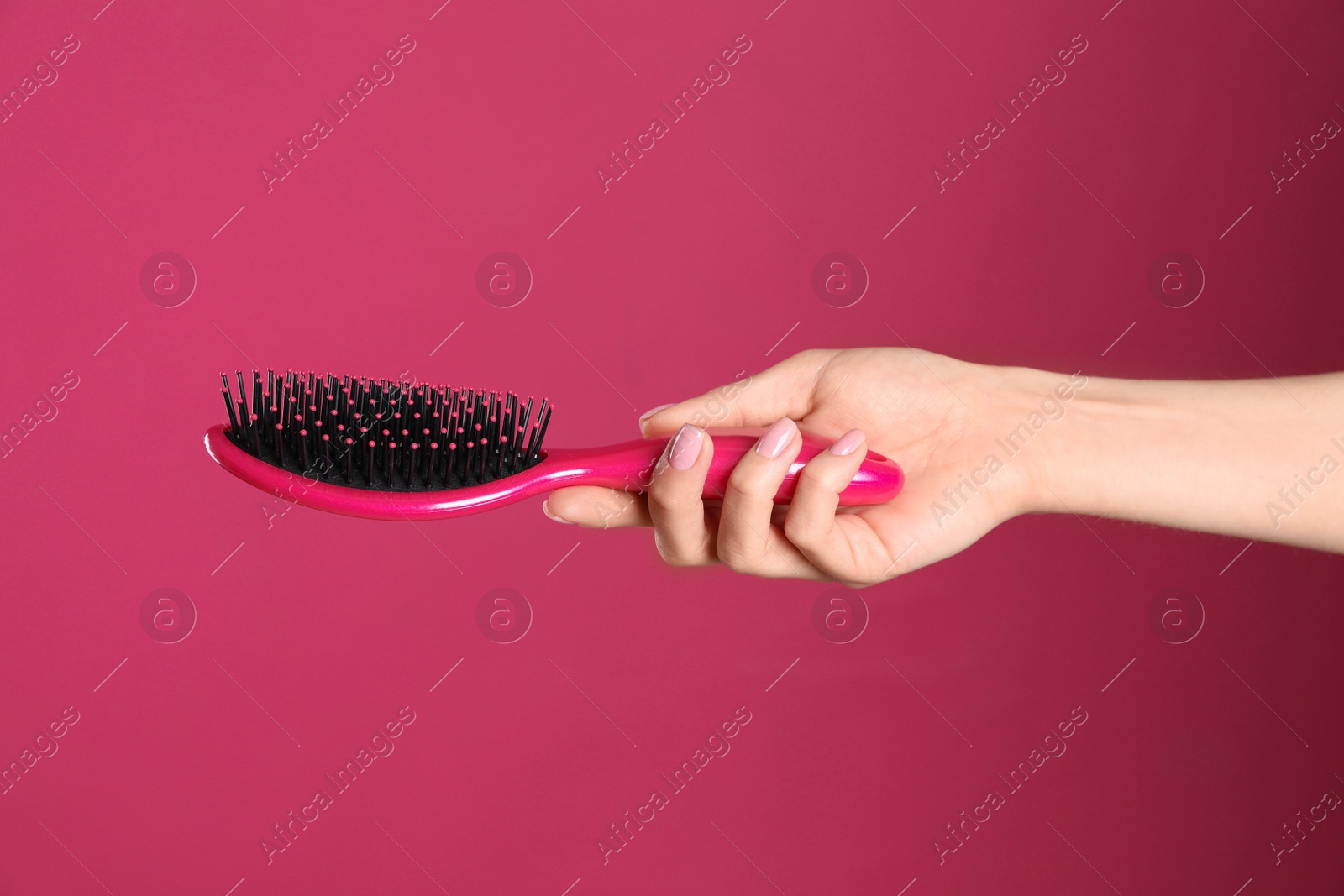 Photo of Woman holding hair brush against crimson background, closeup