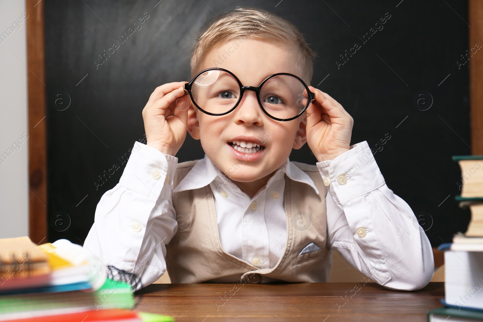 Photo of Cute little child wearing glasses at desk in classroom. First time at school