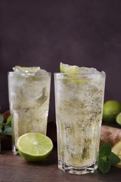 Glasses of tasty ginger ale with ice cubes and ingredients on wooden table