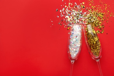 Photo of Shiny confetti spilled out of champagne glasses on red background, flat lay. Space for text