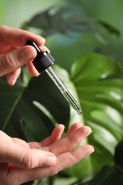 Photo of Woman applying cosmetic serum onto fingers on blurred background, closeup