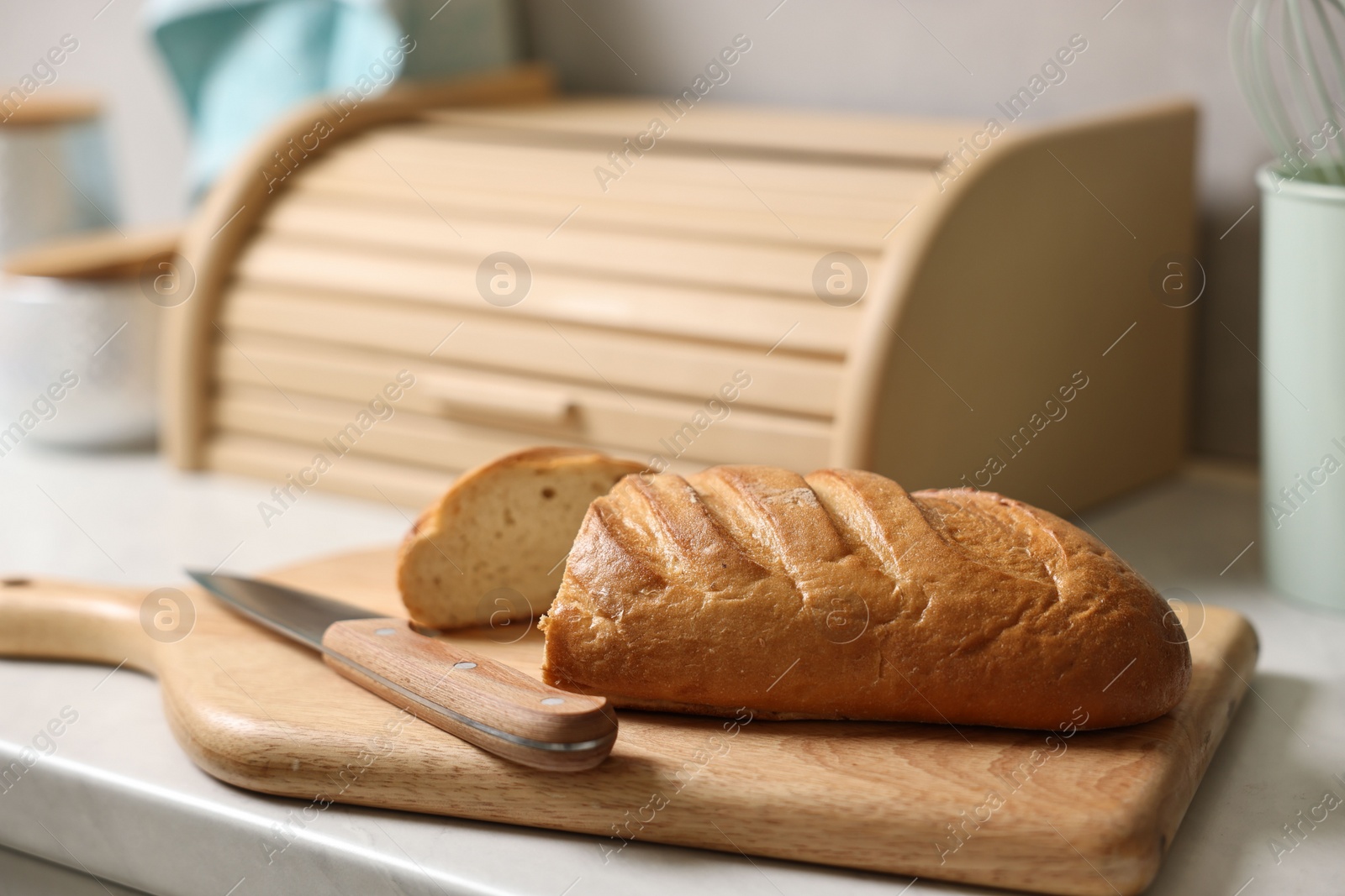 Photo of Wooden bread basket, freshly baked loaf on white marble table in kitchen