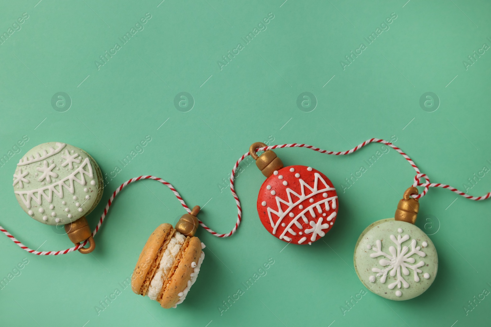 Photo of Beautifully decorated Christmas macarons with rope on turquoise background, flat lay. Space for text