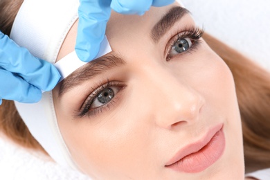 Young woman having professional eyebrow correction procedure in beauty salon