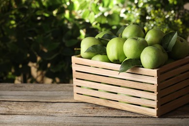 Photo of Crate full of ripe green apples and leaves on wooden table outdoors. Space for text