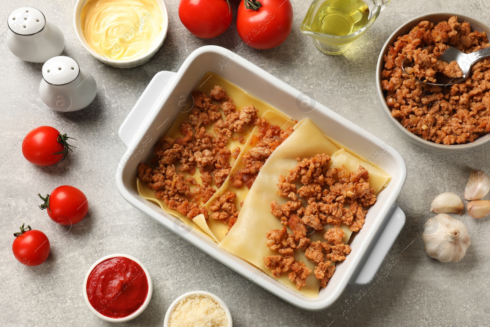 Photo of Cooking lasagna. Pasta sheets, minced meat in baking tray and products on light textured table, flat lay