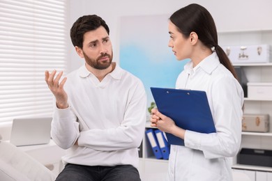 Photo of Doctor with clipboard consulting patient during appointment in clinic