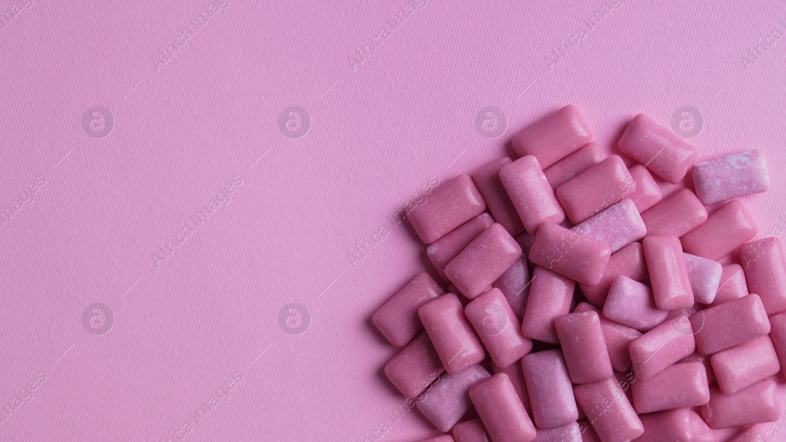 Photo of Heap of tasty sweet chewing gums on pink background, flat lay. Space for text