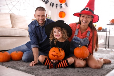 Parents and cute little girl with pumpkin having Halloween party at home