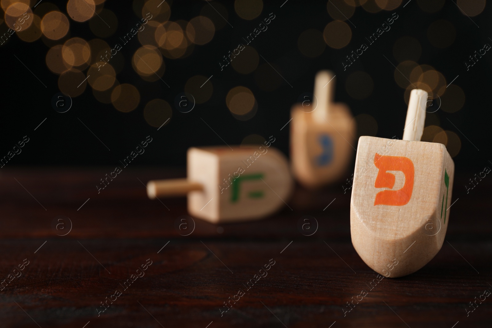 Photo of Hanukkah traditional dreidel with letter Pe on wooden table against blurred lights. Space for text